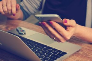 woman with phone in screen and open laptop